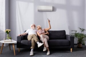 senior-couple-sitting-on-couch-changing-mini-split-temperature-with-remote
