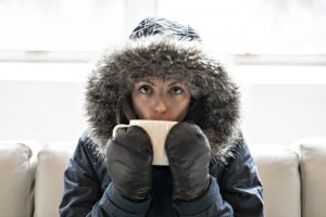 woman-wears-parka-on-couch-sips-hot-beverage